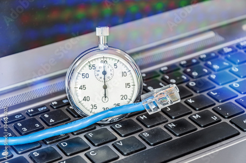 Cable and stopwatch on computer keyboard symbolizing bandwidth of internet connection photo