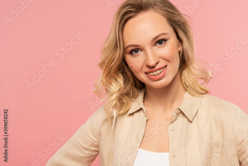 Blonde woman with dental braces smiling at camera isolated on pink