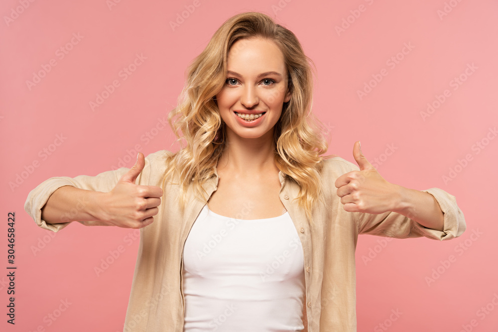 Smiling blonde woman showing thumbs up gesture isolated on pink Smiling blonde woman showing thumbs up gesture isolated on pink