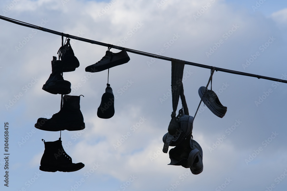 Row of shoes hanging from an electric cable against the backdrop of sky with sunshine. Row of shoes hanging from an electric cable against the backdrop of sky with sunshine.
