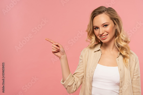 Smiling woman point with finger to side isolated on pink