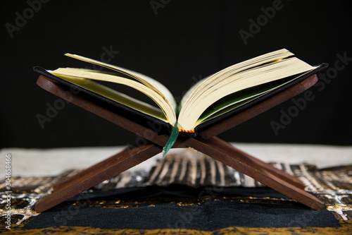 Muslims Islamic Holy Book Quran Majid with Quran wooden stand and Janamaz Prayer Rug and black background photo