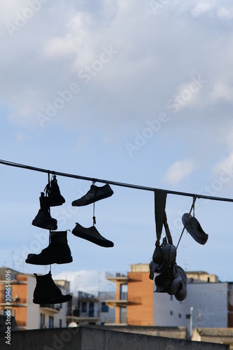 Row of shoes hanging from an electric wire. Background with houses and buildings.