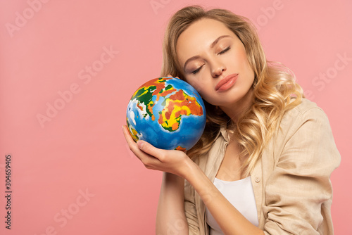 Blonde woman with closed eyes holding globe isolated on pink
