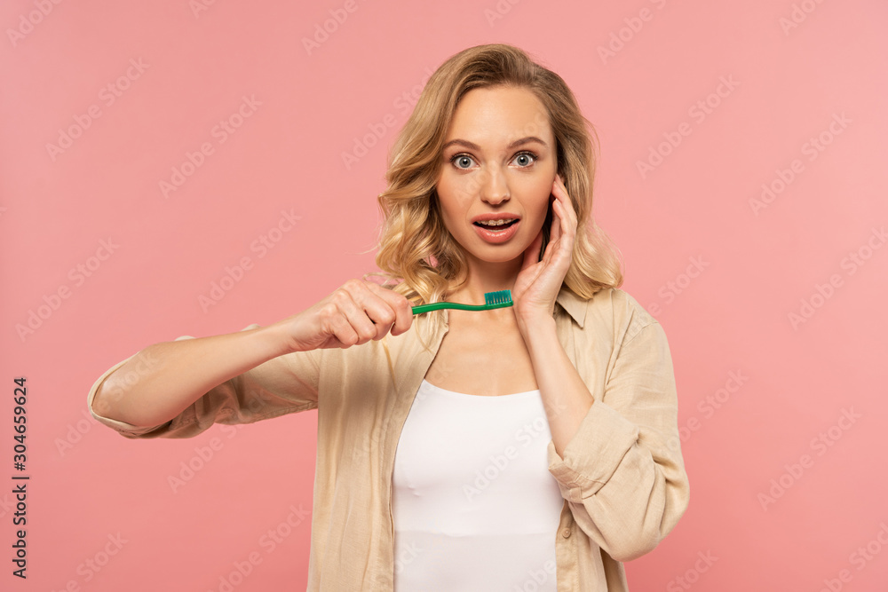 Shocked blonde woman holding toothbrush isolated on pink Shocked blonde woman holding toothbrush isolated on pink