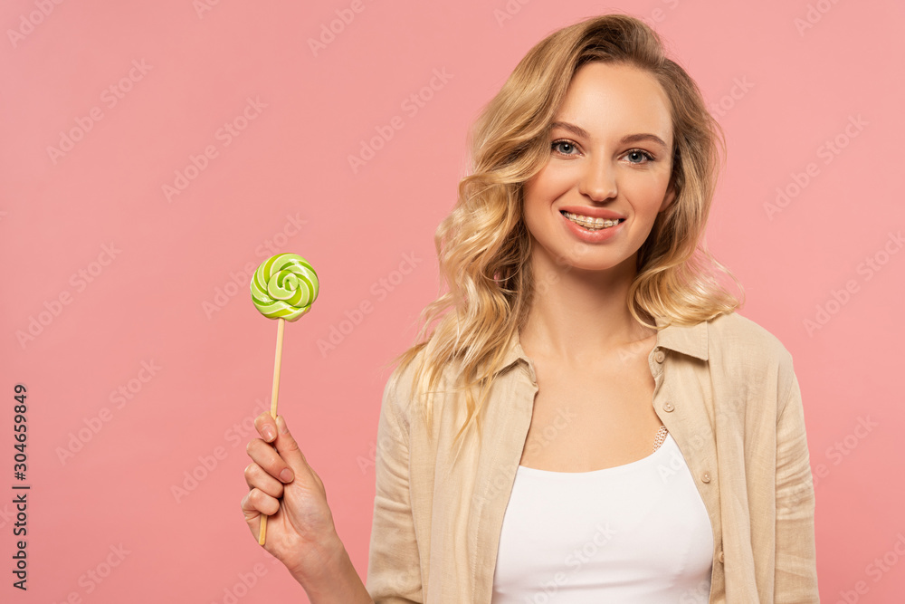 Smiling woman with dental braces holding lollipop isolated on pink Smiling woman with dental braces holding lollipop isolated on pink