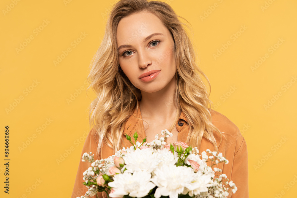 Attractive blonde woman holding bouquet isolated on yellow