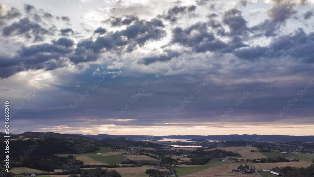 Dark and gloomy clouds swirling above the patchwork of the farm fields and pastures. A pale stripe of the dawn sky visible in a distance. Dark and gloomy clouds swirling above the patchwork of the farm fields and pastures. A pale stripe of the dawn sky visible in a distance.