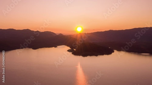 Beautiful autumn sunset over the Kjelavant lake. The orange sun is reflected in the calm waters of the lake engulfing the scene in a warm glow. Dark mountains towering on the background. photo