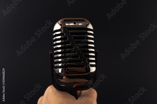 Man holding radio microphone against black background. Shiny music instrument