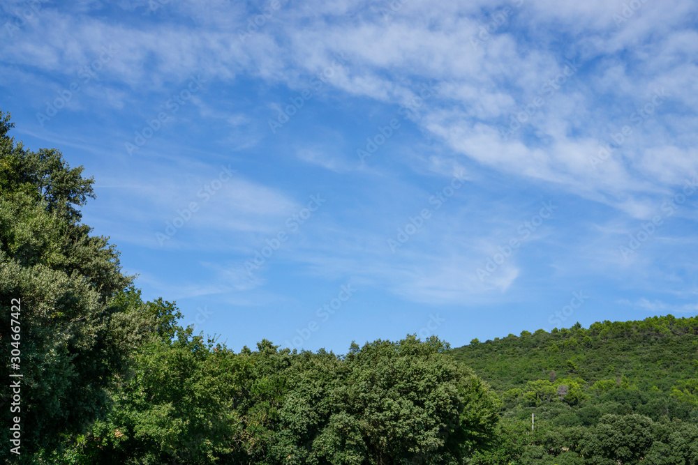 Small wave of beautiful white fluffy clouds on vivid blue sky in a summer time above the mountain and green trees in Vacqueyras village of wine, southeastern France