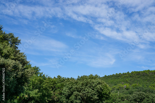 Small wave of beautiful white fluffy clouds on vivid blue sky in a summer time above the mountain and green trees in Vacqueyras village of wine, southeastern France
