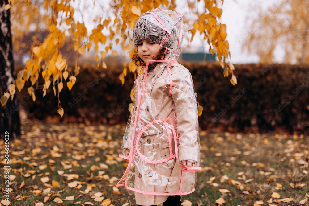 Happy funny child girl wearing transparent raincoat outdoor in