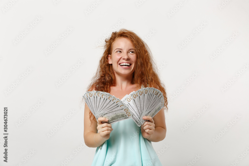 Young laughing redhead woman girl in casual light clothes posing isolated on white background studio portrait. People lifestyle concept. Mock up copy space. Hold fan of cash money in dollar banknotes. Young laughing redhead woman girl in casual light clothes posing isolated on white background studio portrait. People lifestyle concept. Mock up copy space. Hold fan of cash money in dollar banknotes.