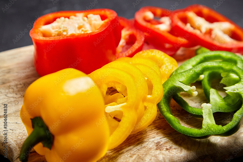 Slices of red, green, and yellow bell peppers on a wooden cutting board, closeup. Sliced sweet peppers in different colors, vegetable salad ingredient, cooking healthy food Slices of red, green, and yellow bell peppers on a wooden cutting board, closeup. Sliced sweet peppers in different colors, vegetable salad ingredient, cooking healthy food