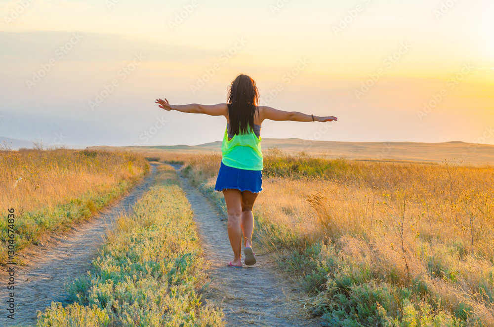 A woman walks along the road in a field in summer.