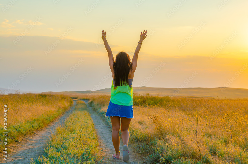 A young girl is walking along the road in a field in summer.Greeting to the sun. A young girl is walking along the road in a field in summer.Greeting to the sun.