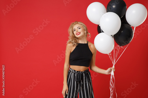 Stunning young woman girl in black clothes posing isolated on bright red wall background in studio. New Year 2020 birthday holiday party concept. Mock up copy space. Celebrating, holding air balloons.