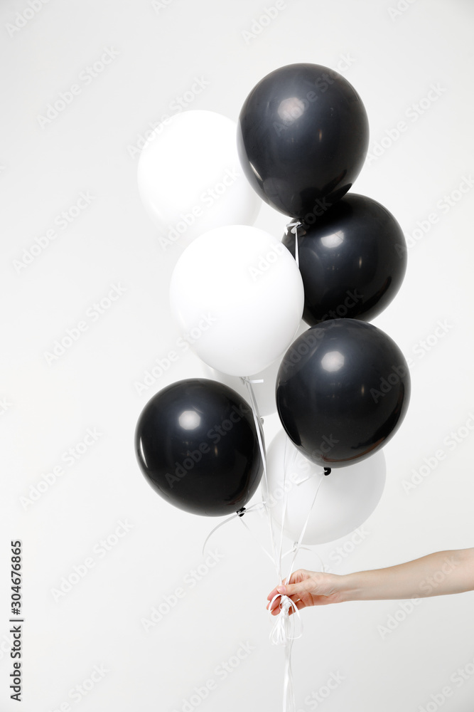 Close up cropped photo of female hold in hand bunch of black and white air balloons isolated on white wall background in studio. Birthday holiday party people lifestyle concept. Mock up copy space. Close up cropped photo of female hold in hand bunch of black and white air balloons isolated on white wall background in studio. Birthday holiday party people lifestyle concept. Mock up copy space.