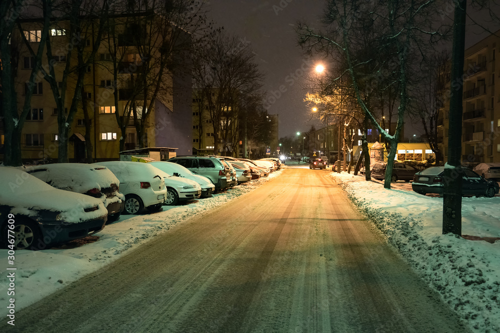 traffic in the city at snowy winter night. Snow-covered cars standing in the parking lot.