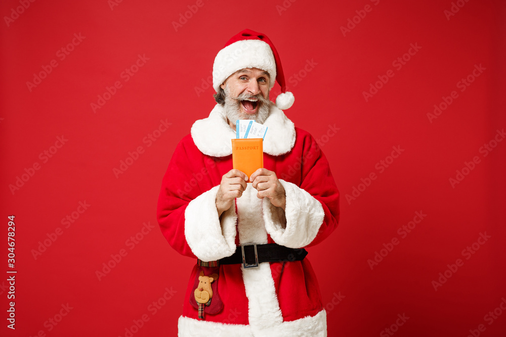 Excited elderly gray-haired mustache bearded Santa man in Christmas hat posing isolated on red background. Happy New Year 2020 celebration holiday concept. Mock up copy space. Holding passport ticket. Excited elderly gray-haired mustache bearded Santa man in Christmas hat posing isolated on red background. Happy New Year 2020 celebration holiday concept. Mock up copy space. Holding passport ticket.
