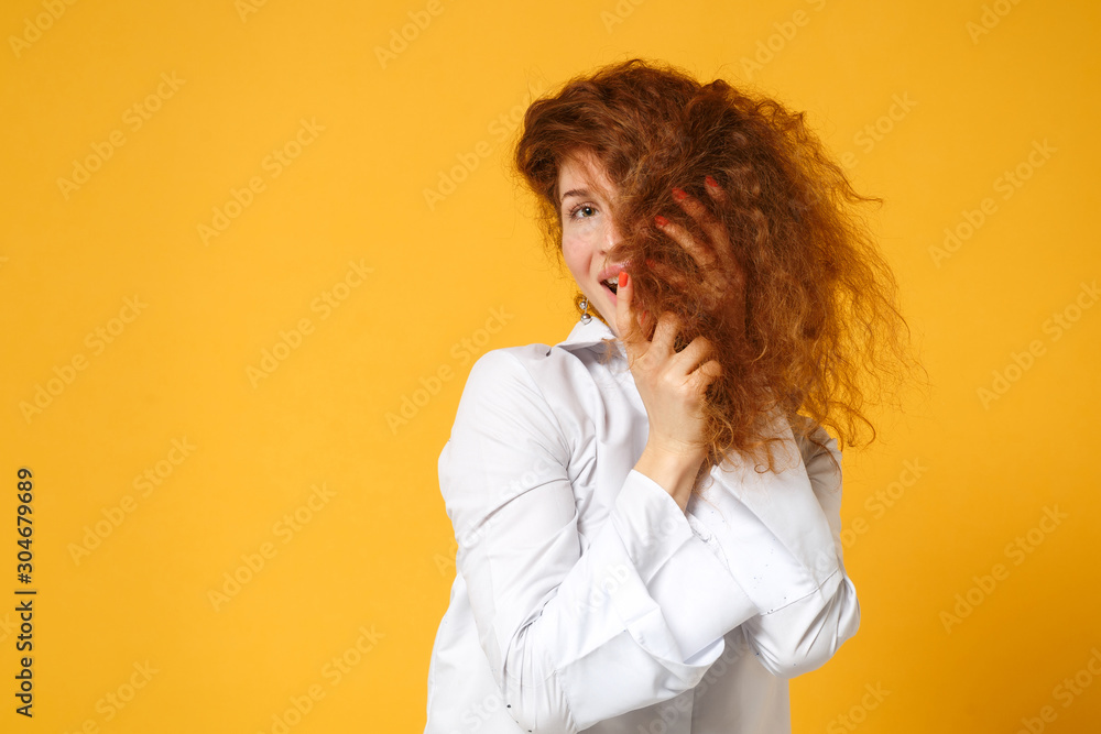 Cheerful young redhead woman girl in white shirt posing isolated on yellow orange background, studio portrait. People sincere emotions lifestyle concept. Mock up copy space. Covering face with hair. Cheerful young redhead woman girl in white shirt posing isolated on yellow orange background, studio portrait. People sincere emotions lifestyle concept. Mock up copy space. Covering face with hair.