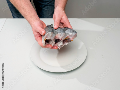 Three clean fresh sea bream on a white plate, Head and guts removed and washed. Ready to cook product. Fishmonger holding fish with his hands.