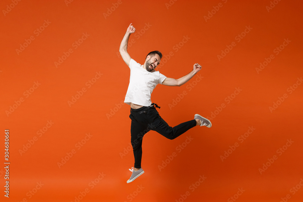 Happy excited young man in casual white t-shirt posing isolated on bright orange wall background studio portrait. People lifestyle concept. Mock up copy space. Having fun jumping doing winner gesture.
