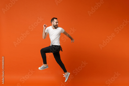 Crazy young man in casual white t-shirt posing isolated on bright orange wall background studio portrait. People lifestyle concept. Mock up copy space. Having fun, fooling around, jumping screaming.