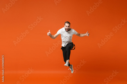 Crazy young man in casual white t-shirt posing isolated on orange wall background studio portrait. People lifestyle concept. Mock up copy space. Having fun, fooling around, jumping, showing thumbs up.