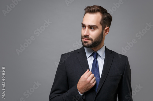 Confident young bearded business man in classic black suit shirt tie posing isolated on grey background studio portrait. Achievement career wealth business concept. Mock up copy space. Looking aside.