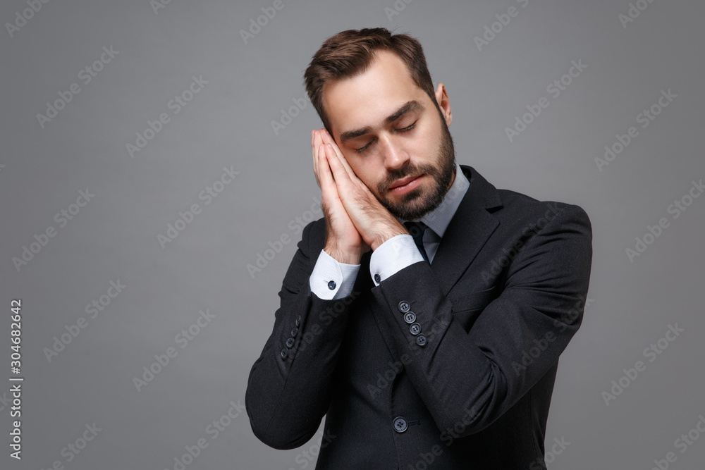 Young bearded business man in classic black suit shirt tie posing isolated on grey wall background. Achievement career wealth business concept. Mock up copy space. Sleep with folded hands under cheek. Young bearded business man in classic black suit shirt tie posing isolated on grey wall background. Achievement career wealth business concept. Mock up copy space. Sleep with folded hands under cheek.