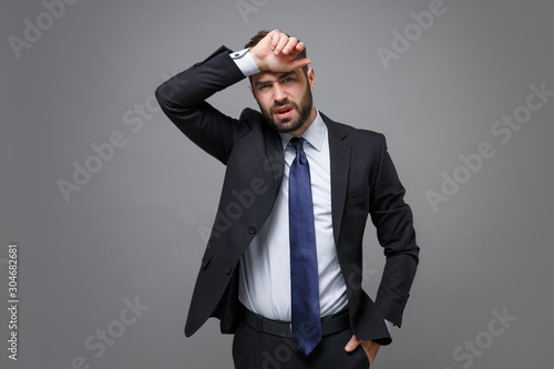 Tableau sur toile Tired exhausted young bearded business man in classic black suit shirt tie posing isolated on grey background