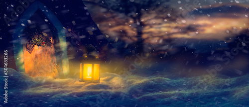 Festive Christmas background scene of a wooden door  wreath and warm glow of a lantern in the snow
