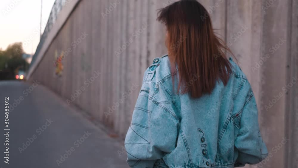 Young woman in blue denim jaket walking. Stylish Fashion Blogger Walking Along Urban Street Young woman in blue denim jaket walking. Stylish Fashion Blogger Walking Along Urban Street