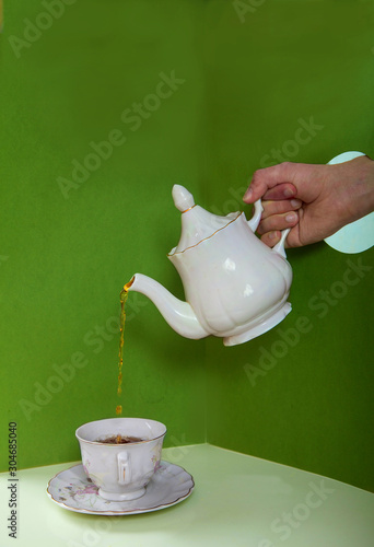 A male hand pours tea from a porcelain teapot into a cup through a hole in paper