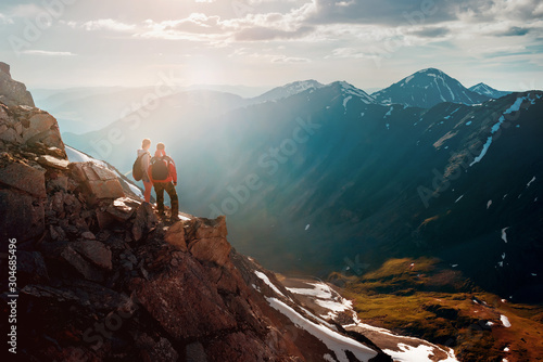 Two hikers stands on cliff in big mountains