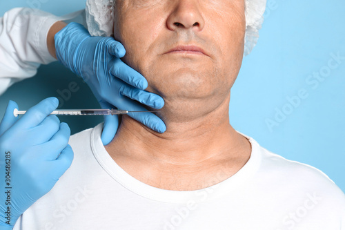 Mature man with double chin receiving injection on blue background  closeup