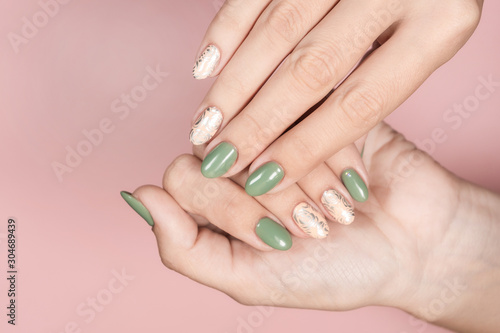 Closeup top view of beautiful perfect manicured female hands isolated on pink pastel background. Fingernails with trendy two colors naildesign decorated with silver stamping on beige nails.