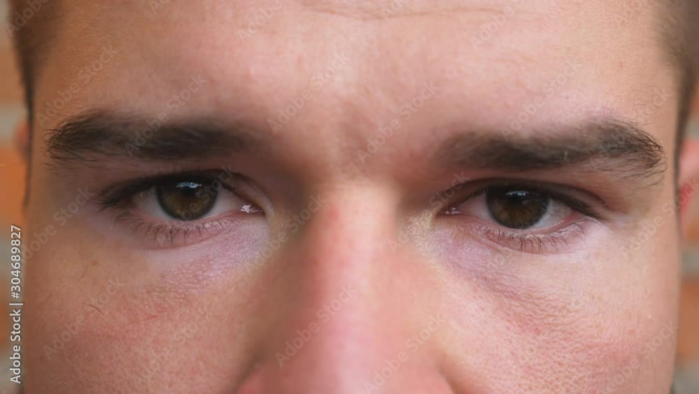 Close up brown eyes of guy staring and blinking with a disappointment sight. Portrait of male face looking into camera. Facial expression of desperate and unhappy young man Close up brown eyes of guy staring and blinking with a disappointment sight. Portrait of male face looking into camera. Facial expression of desperate and unhappy young man