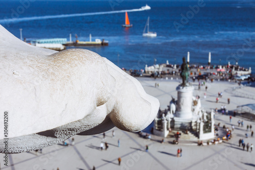 Lisbon, Portugal - May, 30th, 2018 : Detail of foot at the sculpture set atop the Arco da Rua Augusta at Commerce Square with out of focus monument of King José I and Tagus river in background.