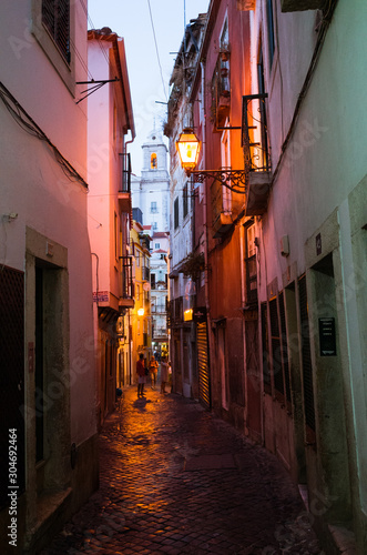 Lisbon, Portugal - July, 24th, 2018 : Night falls on a picturesque alley of the Alfama, the oldest district of Lisbon. Santo Estevao bell tower in background. © Luis Dafos
