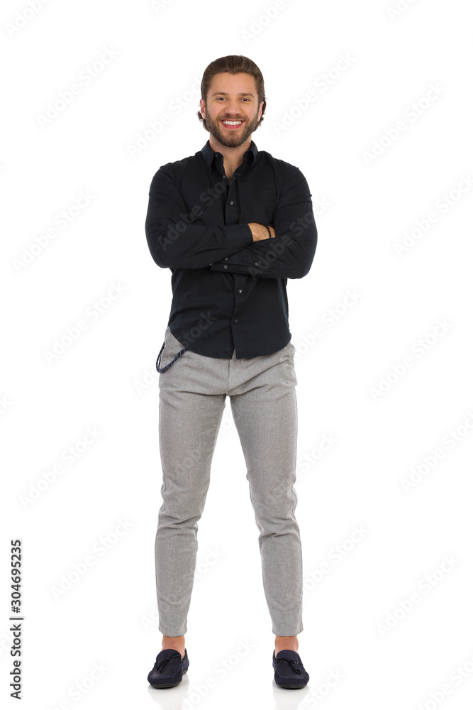 Handsome Man In Gray Trousers, Moccasins And Black Shirt Is Standing With Arms Crossed Handsome Man In Gray Trousers, Moccasins And Black Shirt Is Standing With Arms Crossed