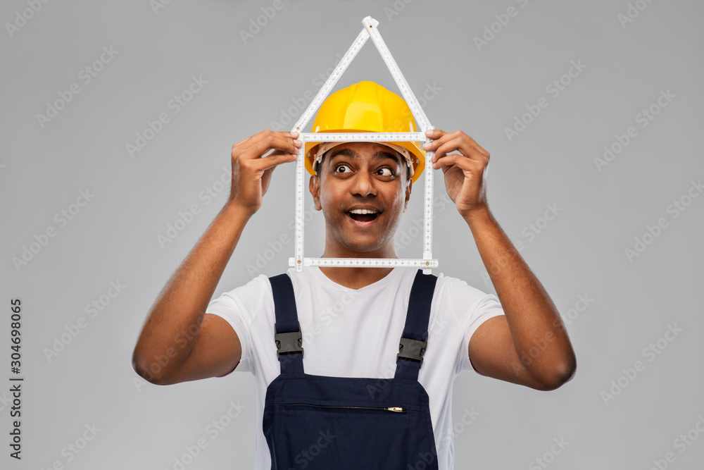 measurement, construction and building - happy smiling indian worker or builder in helmet with folding ruler in shape of home over grey background