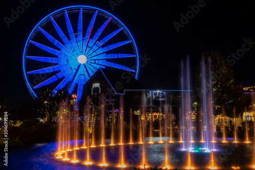 Blue ferris wheel at night with a fountain in the foreground