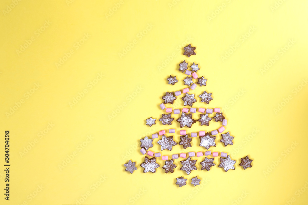 Concept Christmas tree lined with snowflakes gingerbread cookies sprinkled with icing sugar and marshmallows like a garland on a yellow background. Flat lay with copy space. Concept Christmas tree lined with snowflakes gingerbread cookies sprinkled with icing sugar and marshmallows like a garland on a yellow background. Flat lay with copy space.