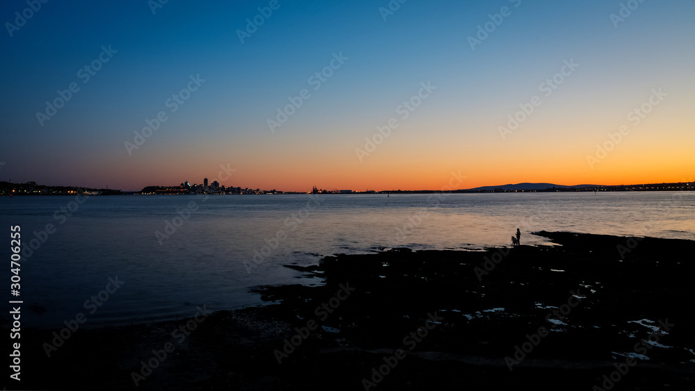Quebec city shadow at the horizon as the colors of sunset cover the sky, while two people admire the landscape from the shore, Quebec, Canada