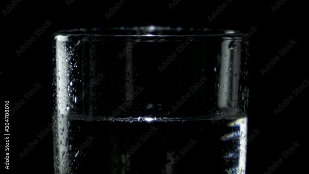 Close-up of a wet glass of water spinning in the dark Close-up of a wet glass of water spinning in the dark