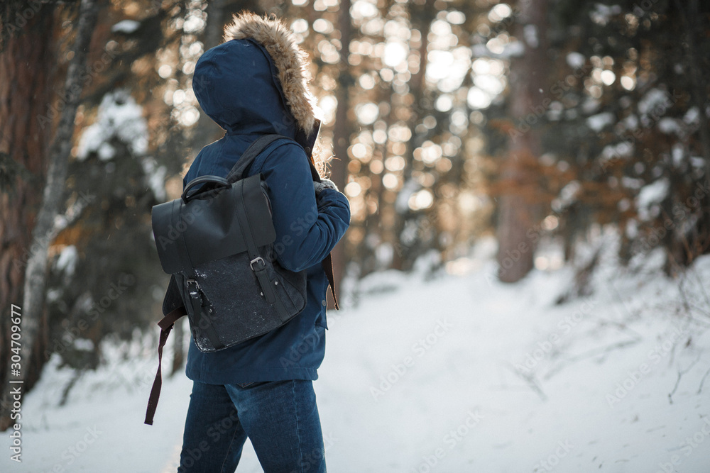 Young woman in warm clothes with backpack walking in winter forest. Back view