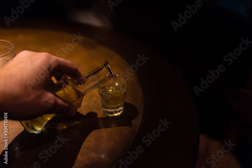 Filling up a snap shot with traditional Greek rakomelo (raki with honey) in a wooden table with low light